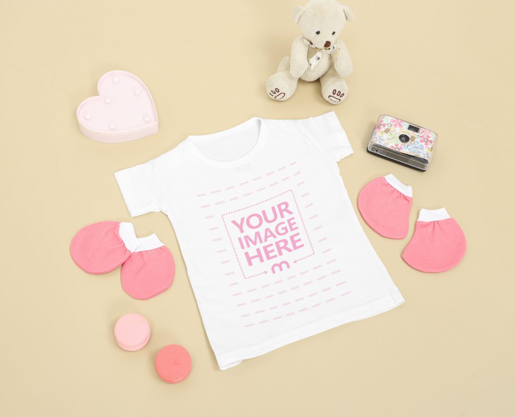 a baby's shirt on a yellow background. Next to it is a bear, a heart and pink gloves and socks
