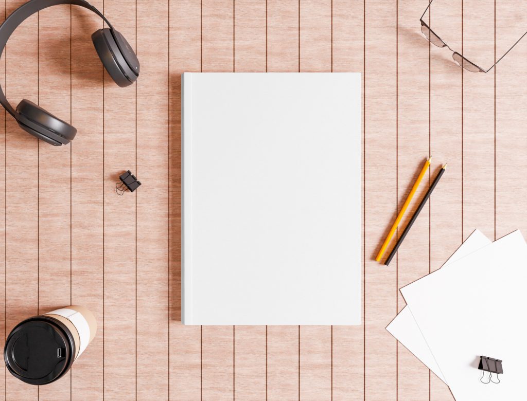 White Note Book on a brown Table with glasses, headphones and a cup of coffee.