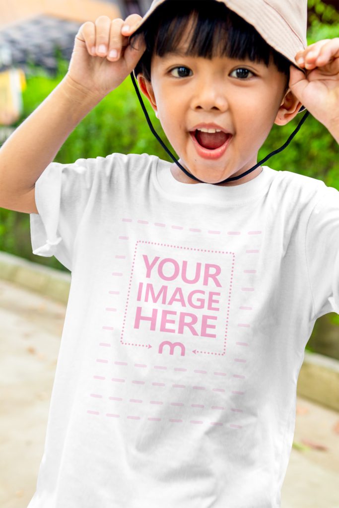 happy boy stands outside with a hat on his head. holds the hat with his hands.