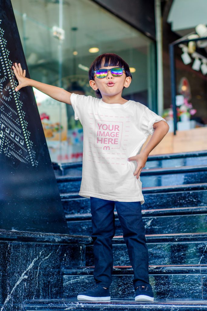 the cool boy is standing on the stairs. he is wearing sunglasses, a t-shirt and blue jeans.