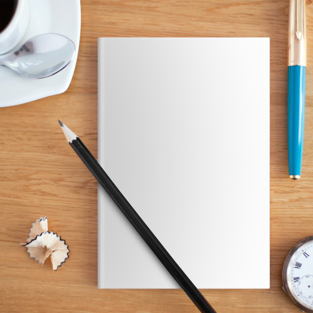 The notebook is on a wooden table with a cup of coffee, a pen and a clock. The pencil is on the notebook.