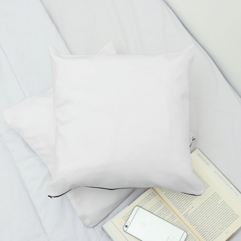 Two pillows on the bed with a book and a phone.