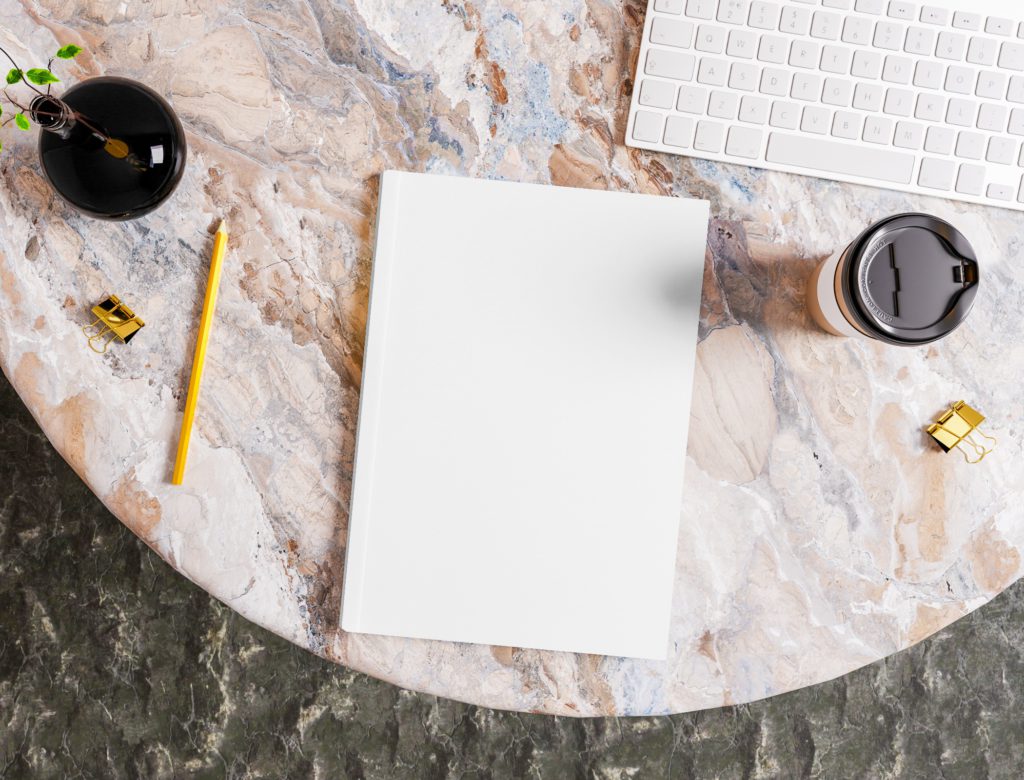 The Journal is on a stone table with a keyboard, a coffee cup and a vase. There are paper holders on the side.